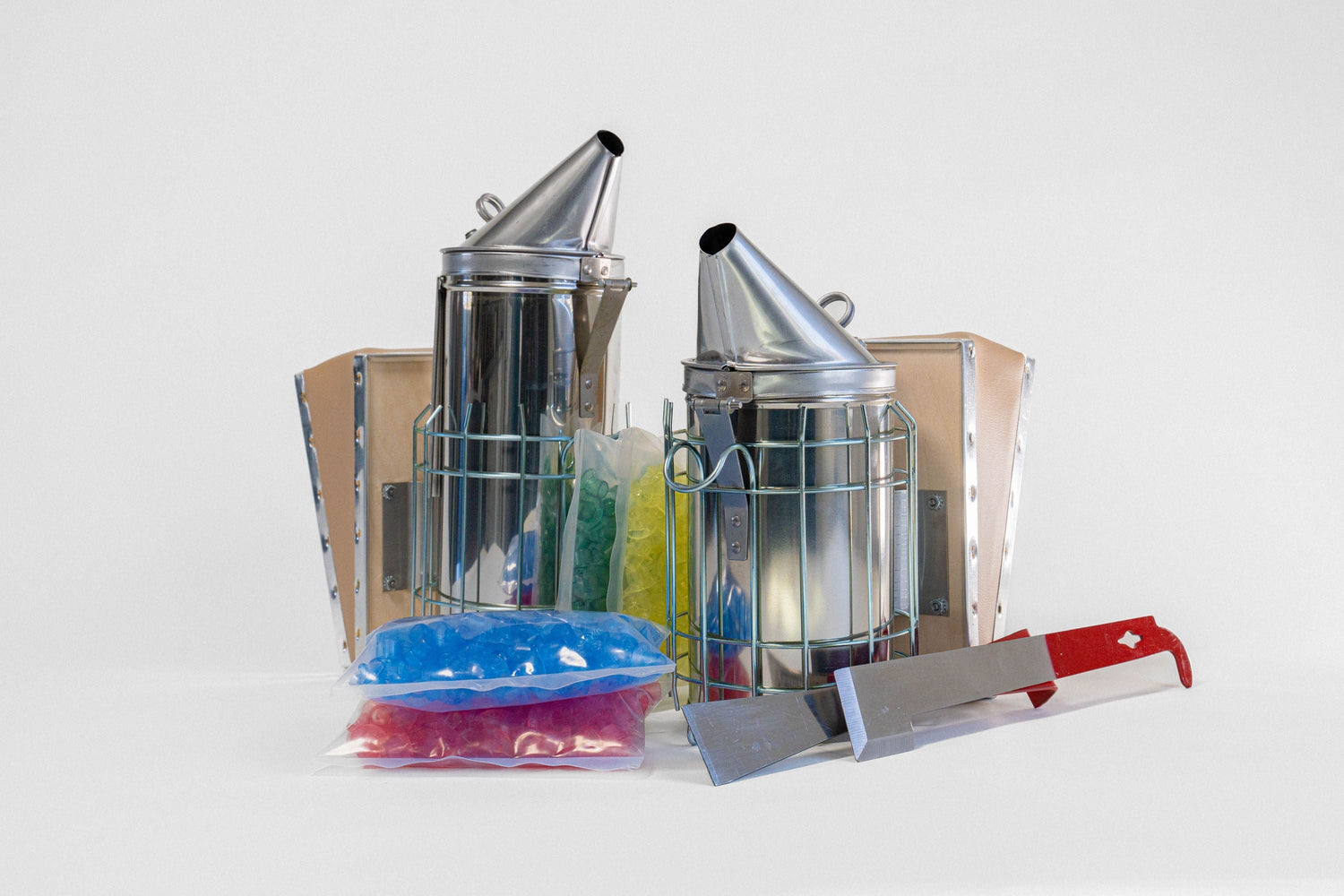 A collage of beekeeping tools, including two smokers, metal hive tools, and plastic queen cell cups on a white background