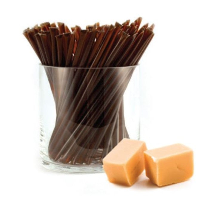 A glass jar of liquid honey stixs, in the flavour caramel on a white background.