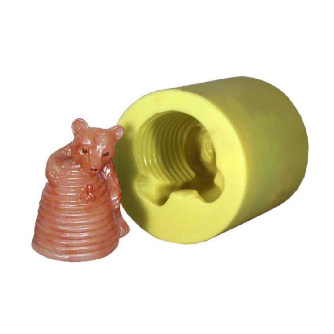 A candle shaped like a bear clutching a beehive next to its corresponding silicone mold.