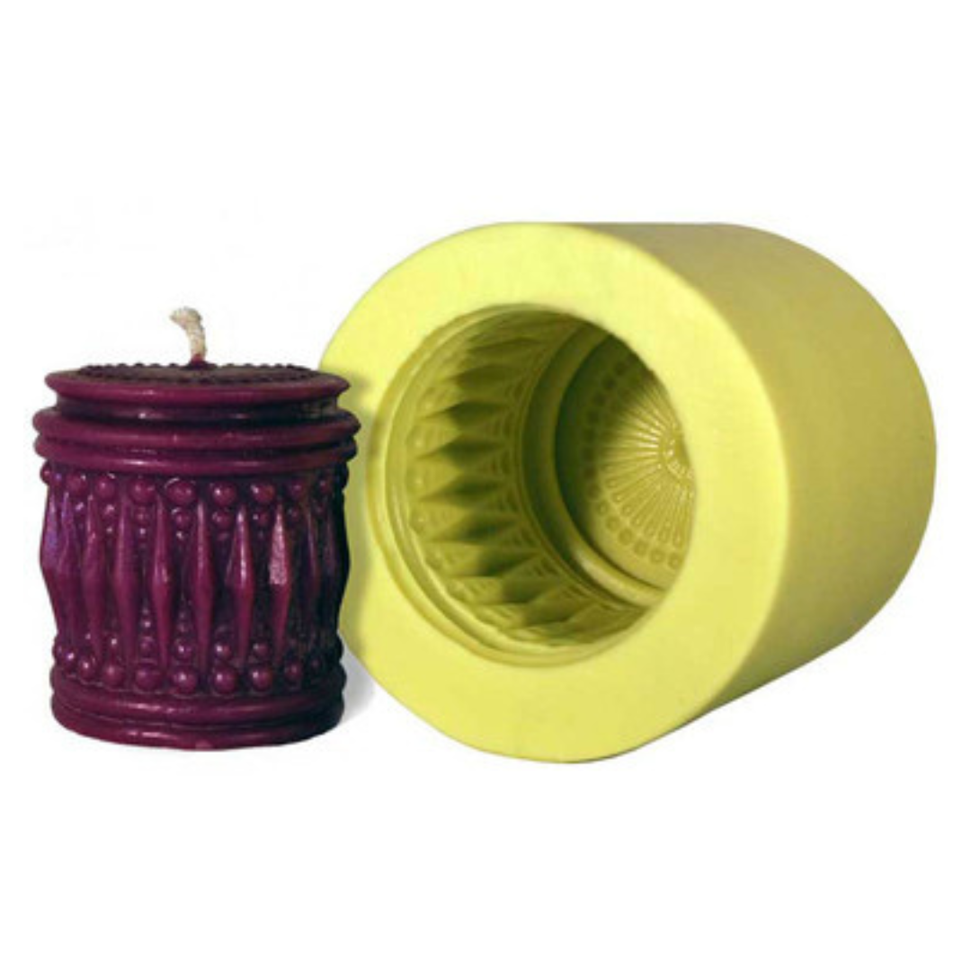 A yellow candle mold with intricate designs, alongside a purple candle with a similar design on a white background