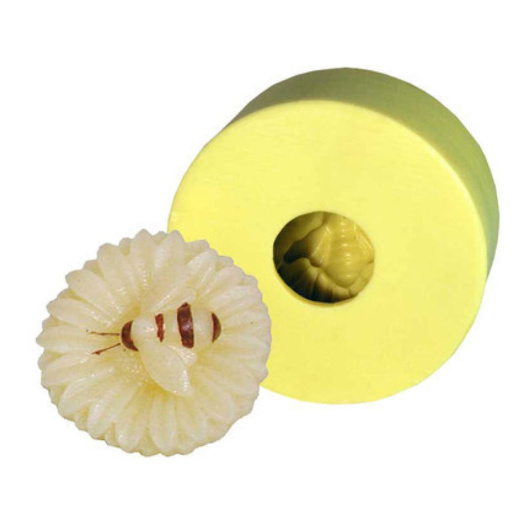 A yellow candle mold in the shape of a sunflower with a bee in the center, alongside a small sample candle made with the mold on a white background