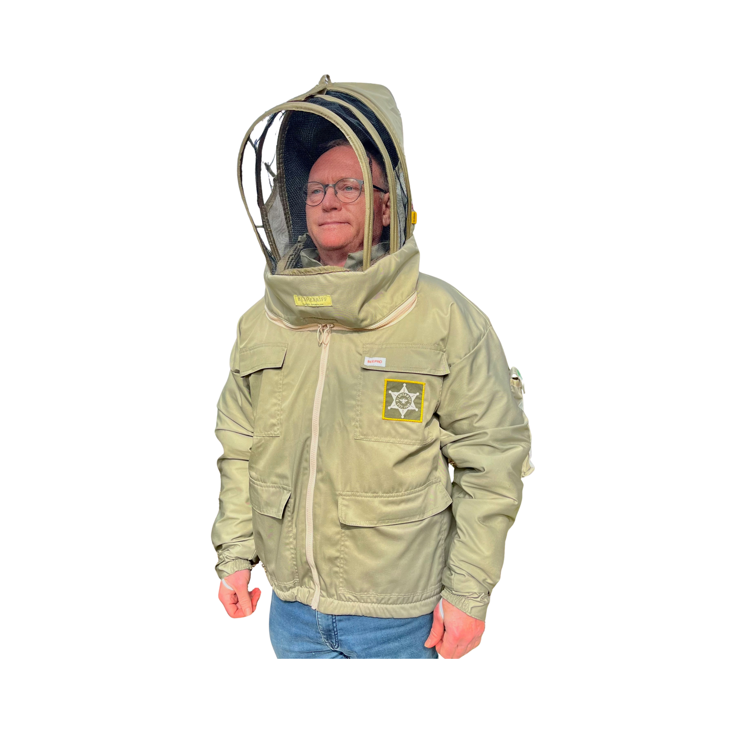 A person wearing a light olive-beige beekeeping jacket with a clear mesh hood and face shield, blue jeans, and glasses, shown against a plain white background.