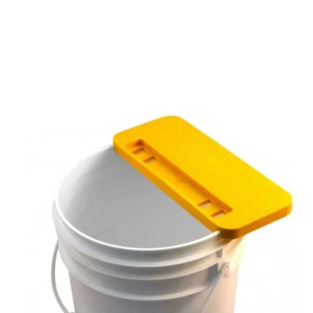 A yellow combcapper placed on top of a white 5-gallon bucket, designed to hold honey frames.