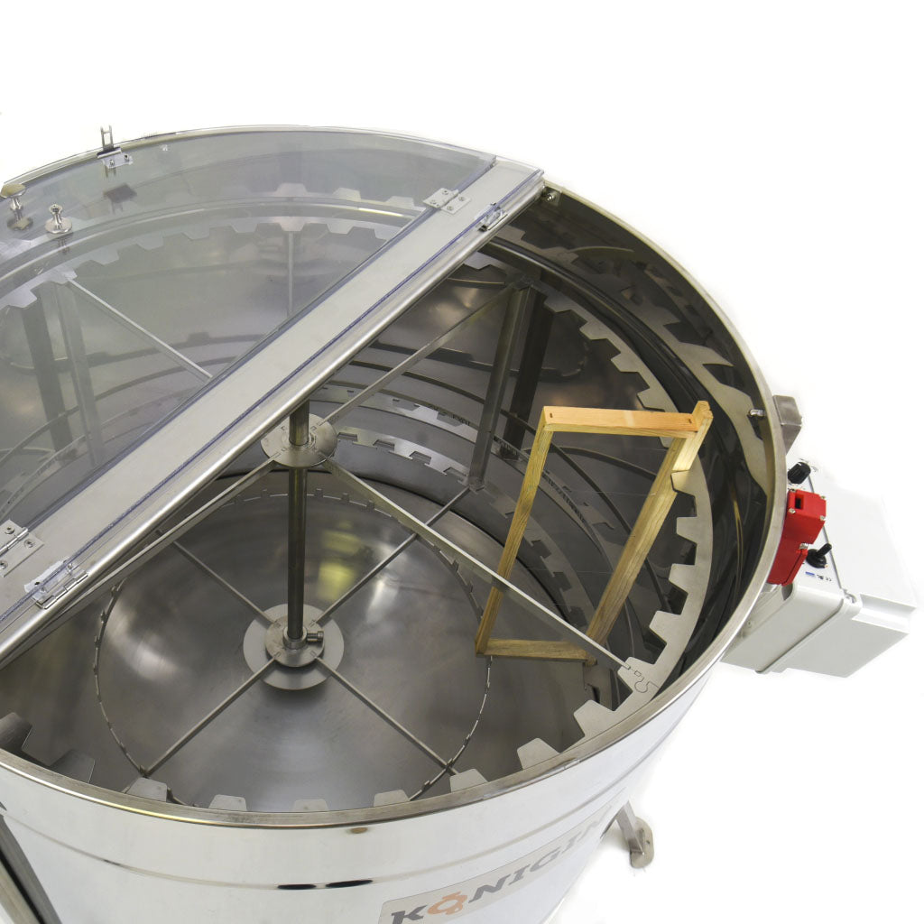 A close up of a metal, radial motorized honey extractor with capacity for 28 frames with the lid opened to expose the interior on a white background
