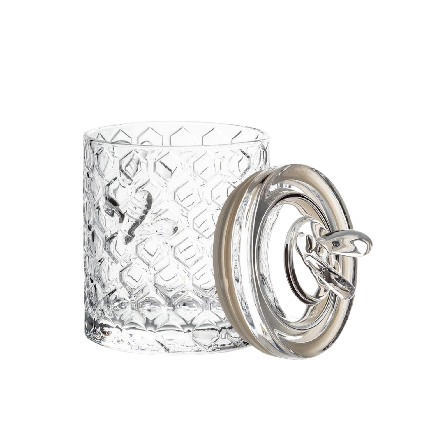 A glass honeycomb jar with its matching glass resting against its right side on a white background. 