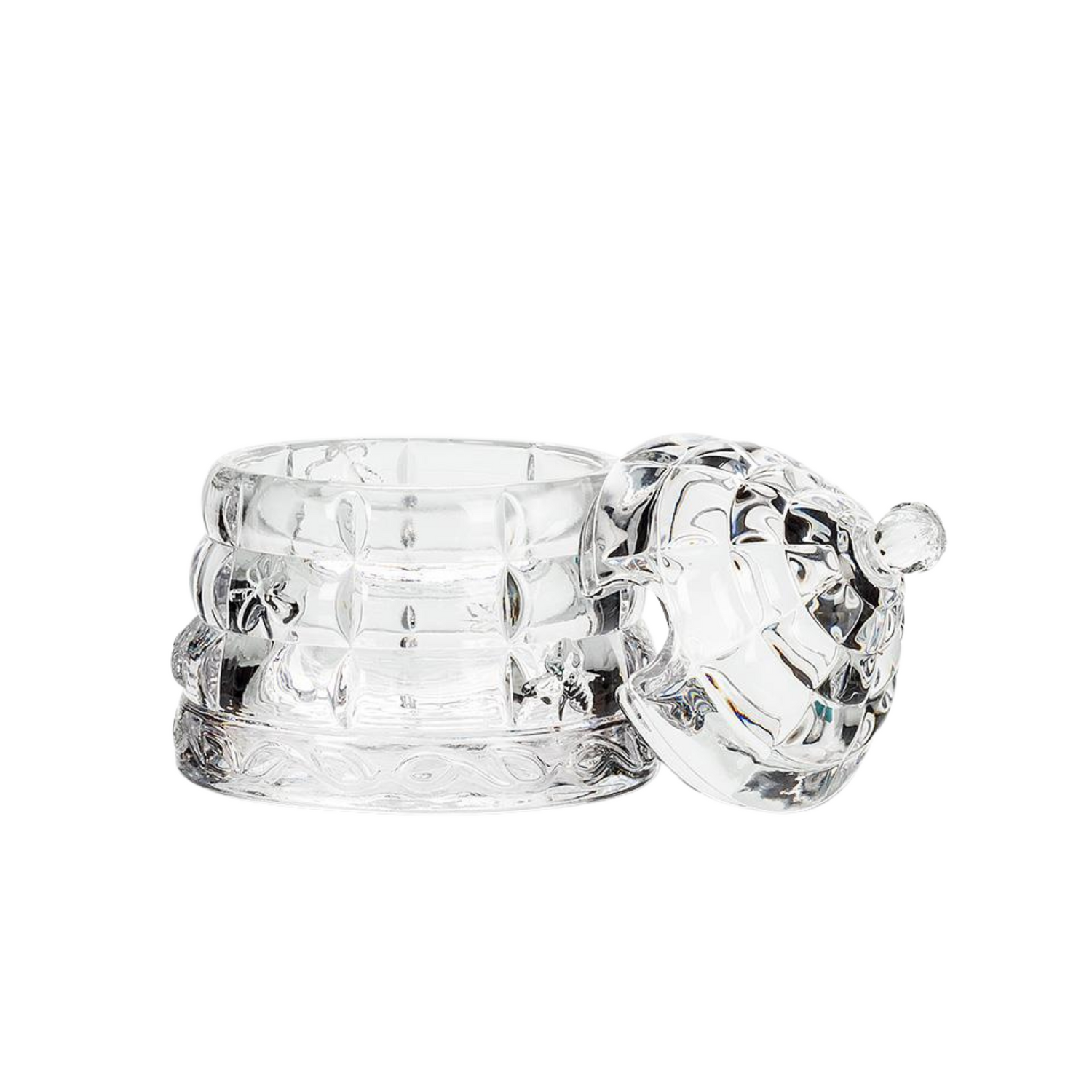 A glass honeypot beehive with its matching lid resting against it on its right side on a white background