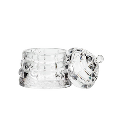 A glass honeypot beehive with its matching lid resting against it on its right side on a white background