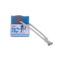 A soap bar with a rope, featuring a blue and brown coloring with a white rope threaded through it and a white paper label.