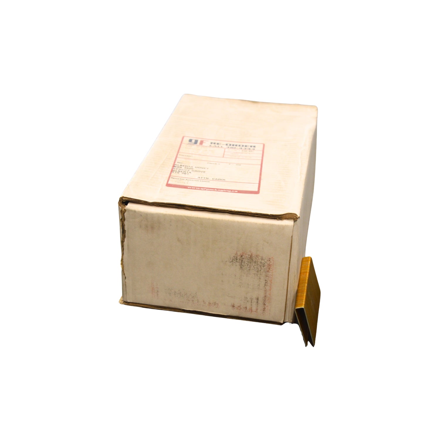 A light brown cardboard box with a white and red label on top, shown on a plain white background with a row of staples laying against it. 
