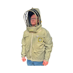 A person wearing a light olive-beige beekeeping jacket with a clear mesh hood and face shield, blue jeans, and glasses, shown against a plain white background.
