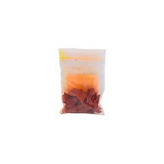 A small clear plastic pouch containing orange dye chips shown on a plain white background.