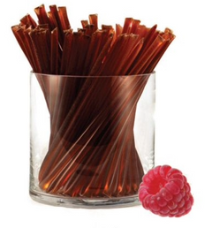 Glass container filled with honey sticks next to a raspberry on a white background