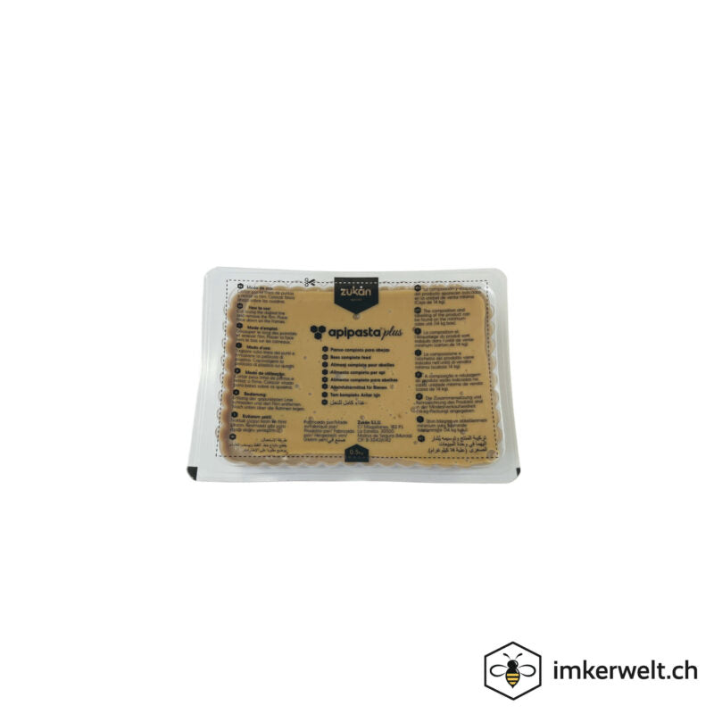 A rectangular 1 kg tray of Apipasta Plus bee feed by Zukán, sealed in clear plastic packaging with printed product information on the top. The fondant is light brown and visible through the packaging.